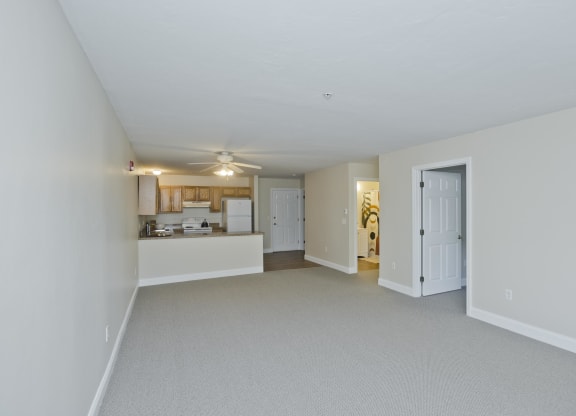 the living room and kitchen of an apartment with white walls and a ceiling fan