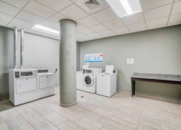 a laundry room with washer and dryers and a table at Cherry Street Lofts in Bridgeport, CT, 06605