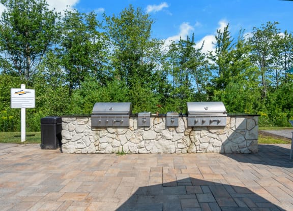 a stone wall with three barbecue pits and trees in the background at The Beacon at Gateway Apartments, Scarborough, ME, 04074