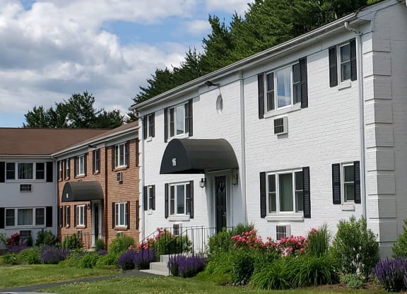 a white and brick building with flowers in front of it at Greenfield Village Apartments, Rocky Hill, Connecticut