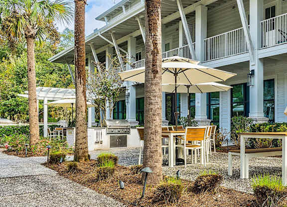A white building with a balcony and a patio with chairs and an umbrella.