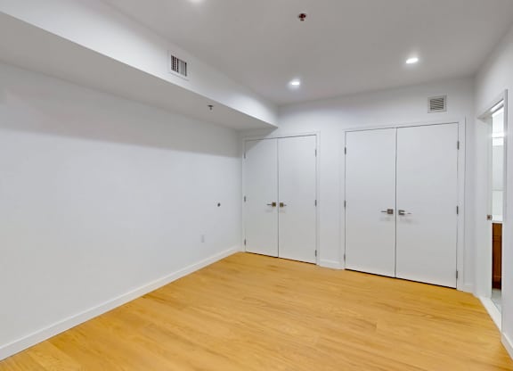 A room with white walls and wooden flooring with three white doors.