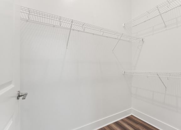 A white closet with a wooden floor and white shelves.