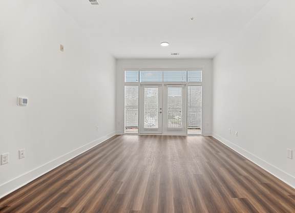 A room with wooden floors and a white wall with a door at the end.