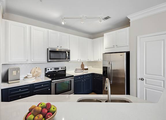 A kitchen with white cabinets and a bowl of apples on the counter.