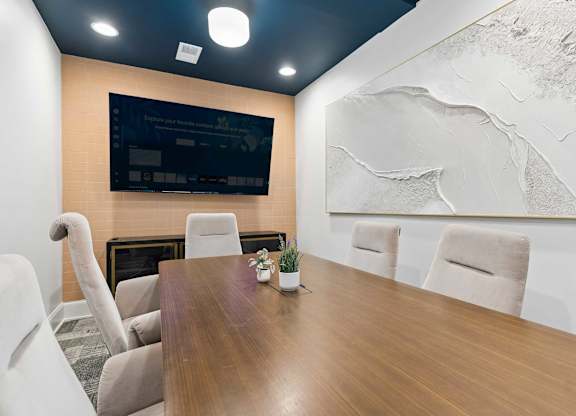 A conference room with a wooden table, chairs, and a large screen on the wall.