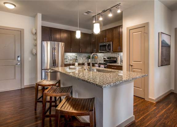 A kitchen with a granite countertop and wooden chairs.