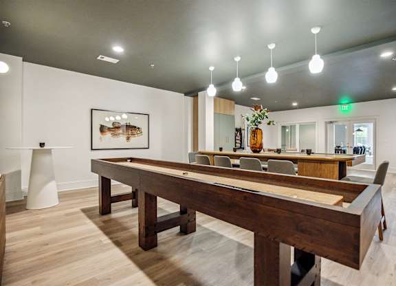 A long wooden table is in the middle of a room with a pool table and a painting on the wall.