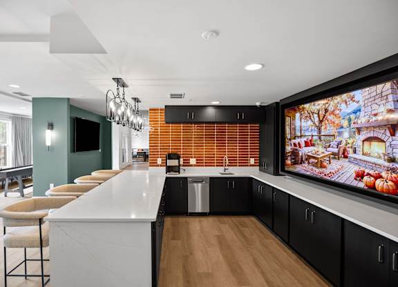 A modern kitchen with a long white island and a large TV mounted on the wall.