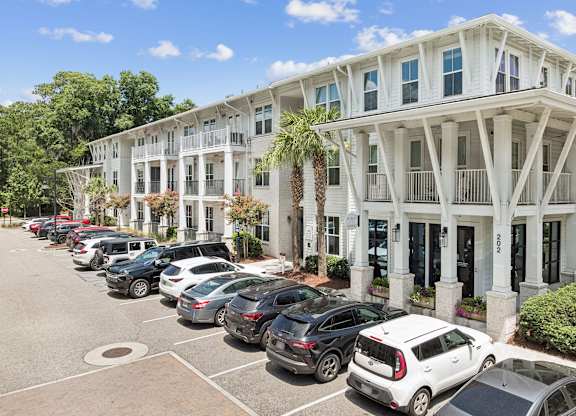 A white building with a row of cars parked in front.
