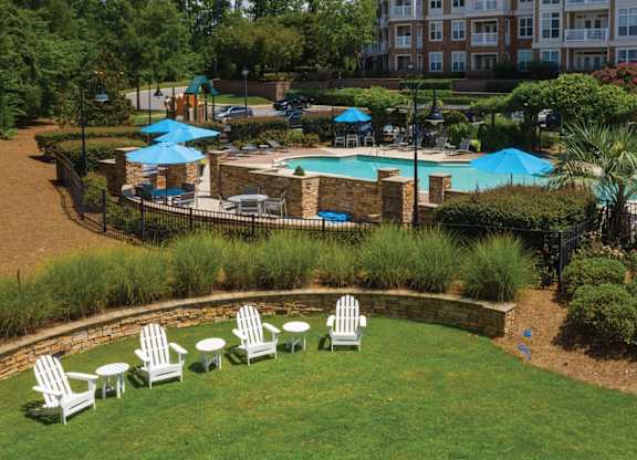 A pool surrounded by a grassy area with chairs and umbrellas.