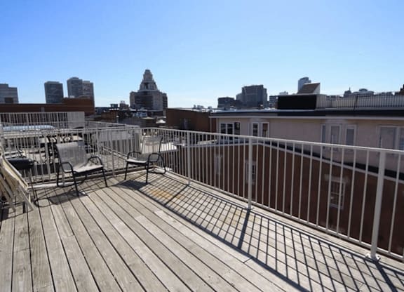 A wooden deck with chairs and a metal railing overlooking a city skyline.