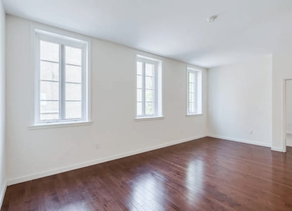 A room with wooden floors and three windows.