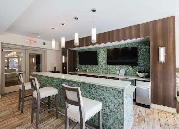 A kitchen with a green backsplash and a bar area with two chairs.