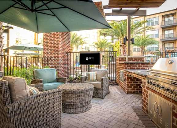 A patio with a grill and chairs under an umbrella.