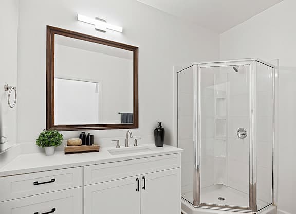 A white bathroom with a mirror, sink, and shower.