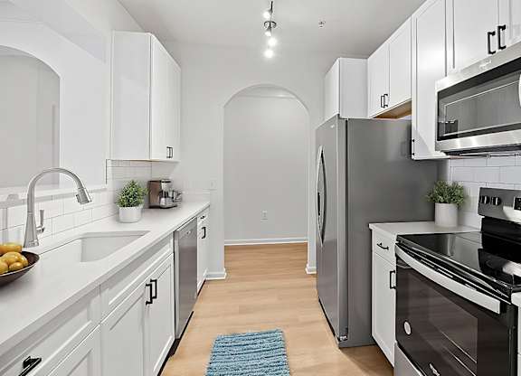 A kitchen with white cabinets and a blue rug on the floor.
