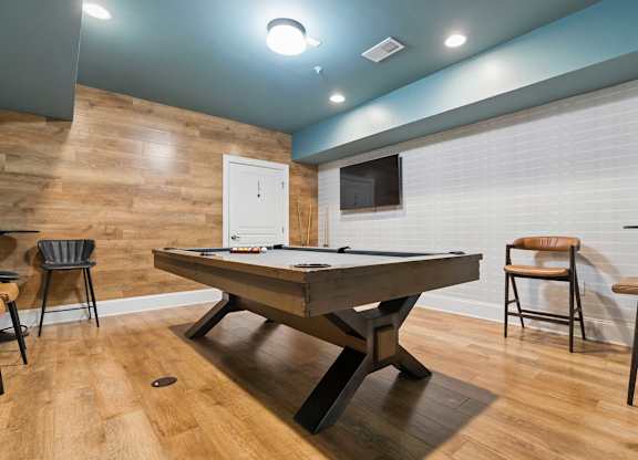 A pool table is in the middle of a room with a wooden floor and a white door.