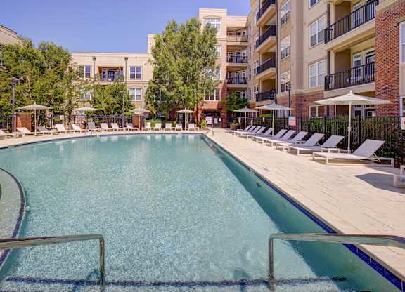 A large swimming pool surrounded by sun loungers and apartment buildings.