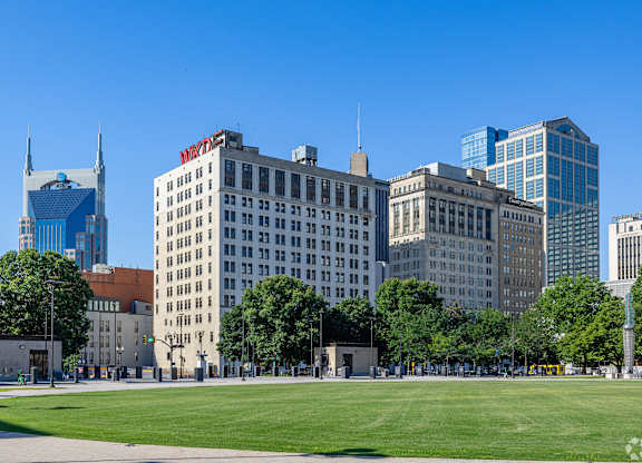 A cityscape with a grassy area in the foreground and buildings of varying heights in the background.