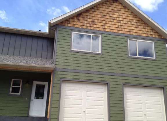 a green house with two white garage doors at Copper Pines, Bozeman