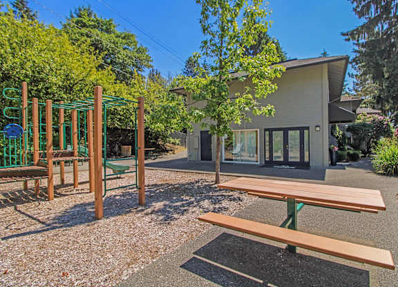 A playground with a slide and a picnic table in front of a house.