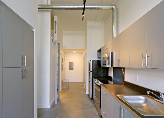 Hallway with concrete floors and at 19th & Mercer, Seattle, WA 98112cabinets on the left and kitchen on the right. A latter on the left side accessing a loft.