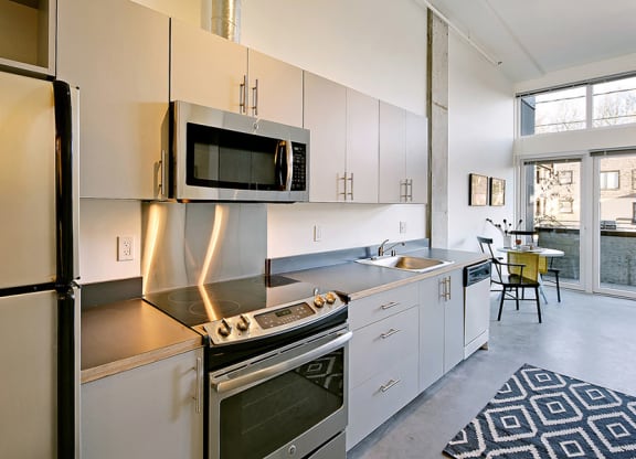 Kitchen with a fridge, oven, microwave, sink and dishwasher from left to right. Stainless steel appliances and a staged seating area.at 19th & Mercer, Seattle Washington