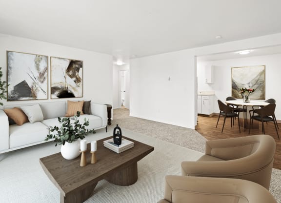 A bright living room with taupe carpets, white walls and staged with a white couch, a coffee table, two chairs and wall art.at North Pointe, Post Falls, ID