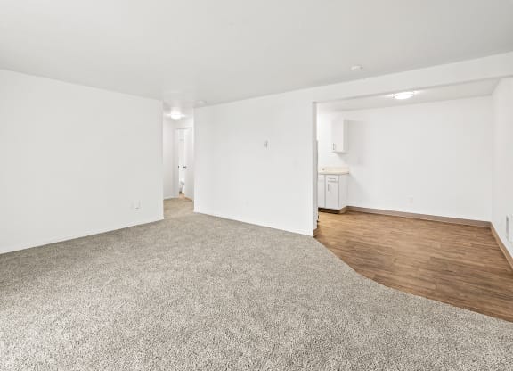 Bright white living room area with taupe carpet, and view of dining area with faux wood flooring at the far right back of the photo.at North Pointe, Post Falls, ID