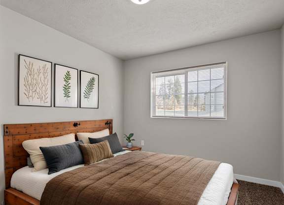 Bedroom with a full bed, decorative pillows, framed artwork, and soft neutral tones at The Overlook Apartments in Post Falls.