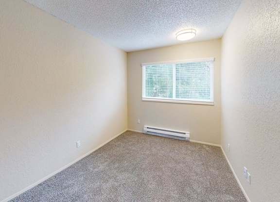 Comfortable bedroom at Peak 88 Apartments in Renton WA featuring soft carpeting, neutral tones, and a large window.