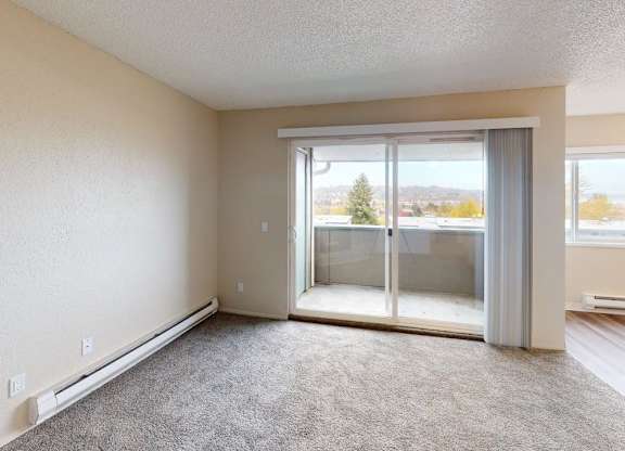 Spacious living room at Peak 88 Apartments Renton WA with plush carpeting, large sliding glass door, and private balcony access.
