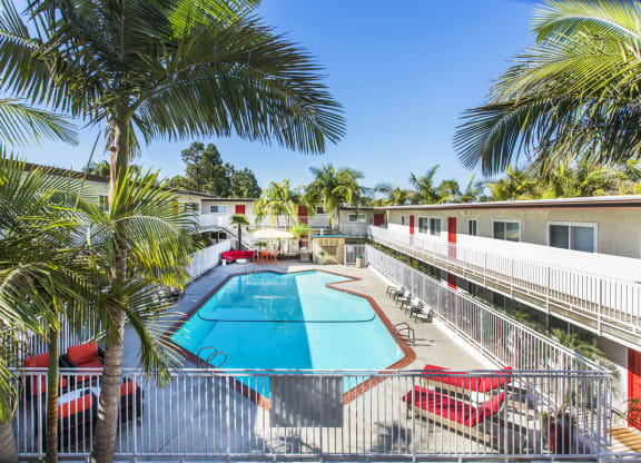 Outdoor swimming pool with sun chairs, a lounge area lined with apartments, and palm trees at Pacific Sands, San Diego, CA