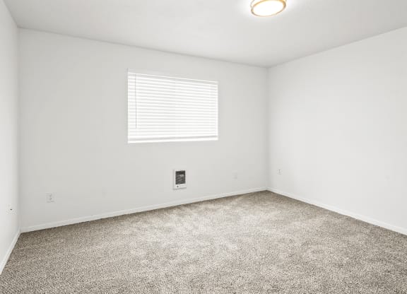 Bright empty bedroom with taupe carpet, white walls and white horizontal blinds on a window on the opposite wall.at North Pointe, Idaho, 83854