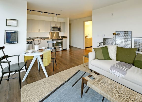 Open layout living space that flows into a dining and kitchen area. Staged with a couch, coffee table, circular dining table and dining chairs.at 19th & Mercer, Seattle, WA 98112