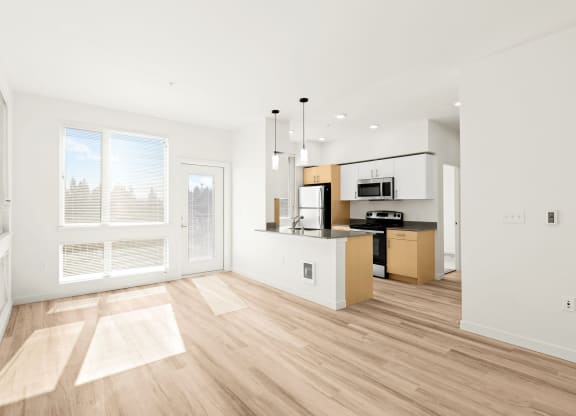 an empty living room with a kitchen and a large window at The Duo, University Place Washington