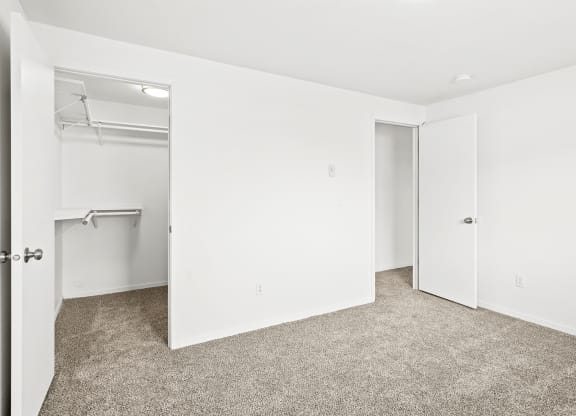 Bright white bedroom with taupe carpet and two open doors. One door leading to hallway, one door leads to walk-in closet with rods at multiple levels.at North Pointe, Idaho