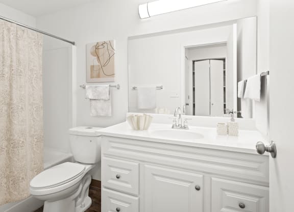 A full bathroom with white vanity sink, cabinet storage, large mirror, a toilet and shower. The linen closet is shown in the mirrors relection.