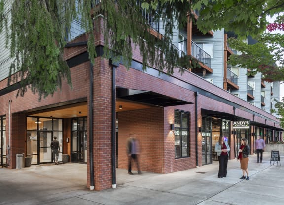 Corner exterior with trees, balconies, and people outside retail spaces at 6 Wood Flats, Lacey, 98503