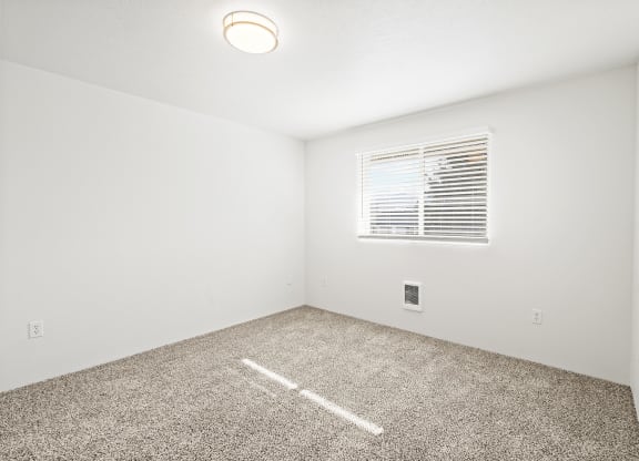 Bright empty bedroom with taupe carpet, white walls and white horizontal blinds on a window on the opposite wall.at North Pointe, Idaho, 83854
