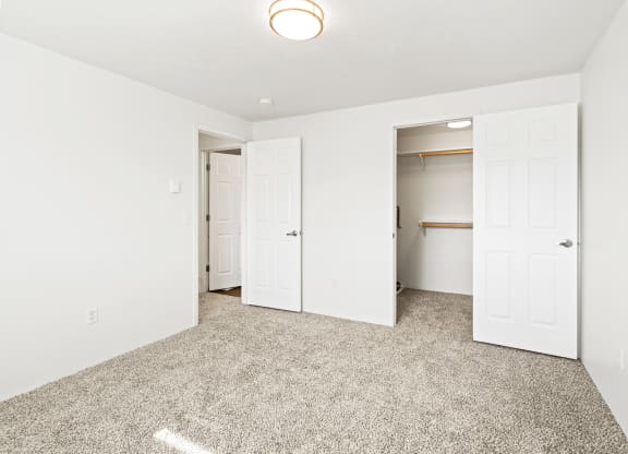Bright white bedroom with taupe carpet and two open doors. One door leading to hallway, one door leads to walk-in closet with rods at multiple levels.at North Pointe, Post Falls Idaho