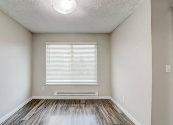 A dining room with taupe walls, wood-like flooring, a large window with blinds on the back wall, and overhead lighting. at Pointe East, Washington, 98424