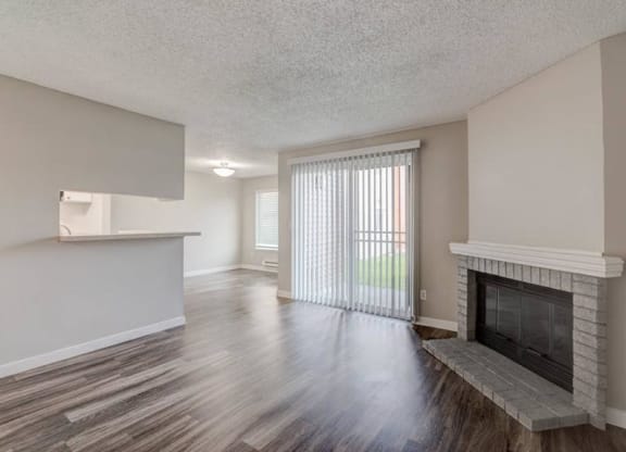 A living room with a fireplace, sliding glass doors to a patio, a kitchen breakfast bar, and a dining room to the left. at Pointe East, Fife, Washington