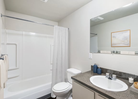 A full bathroom with a vanity sink, cabinet storage, a large mirror, a toilet, and a white shower curtain.at Wildflower, Washington