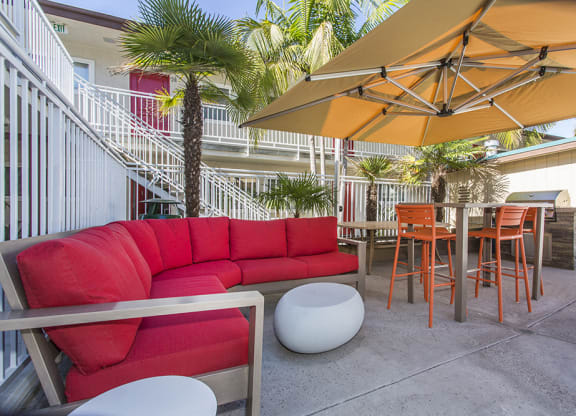 Outdoor resident lounge with a red patio sofa, high table with orange chairs next to the pool, with a gas BBQ at Pacific Sands, San Diego, California