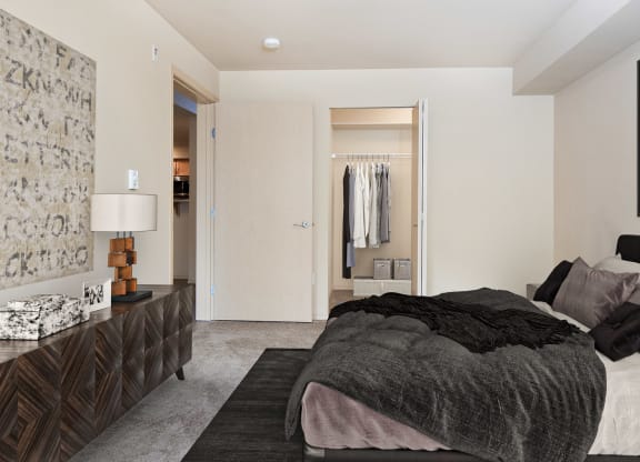 Carpeted bedroom with a queen size bed, a long set of drawers, art on the walls, and a closet with an accordion door at 6 Wood Flats, Lacey, WA
