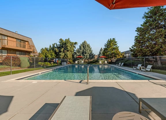 Large swimming pool, lounge chairs, tables, umbrella-covered seating, fenced and surrounded by grass, trees, and bushes.at Castlerock, Wenatchee Washington