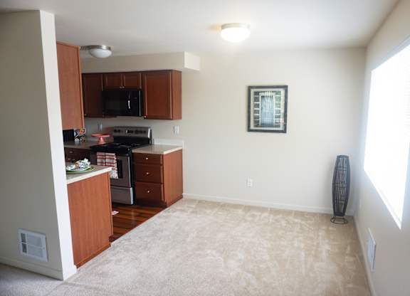 a kitchen and dining area with a carpeted floor and large window at Heritage Grove Apartments in Renton, WA