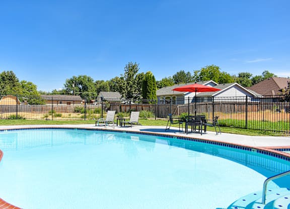 our resort style swimming pool is next to our yard with chairs and an umbrella